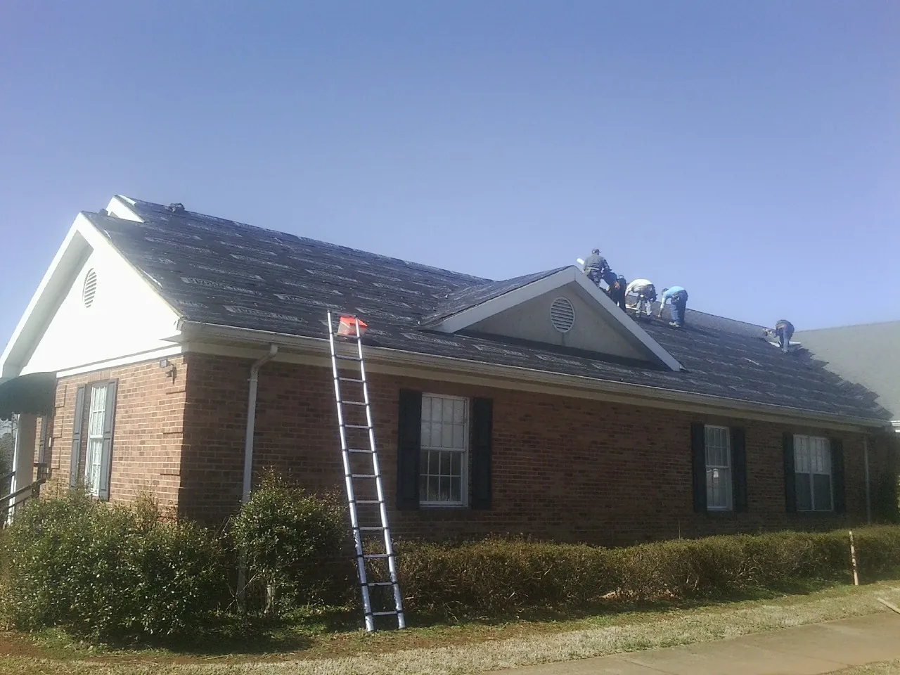 Crew tearing shingles off a brick ranch roof with a ladder set — Emergency Roof Repair work by our crew in Olanta