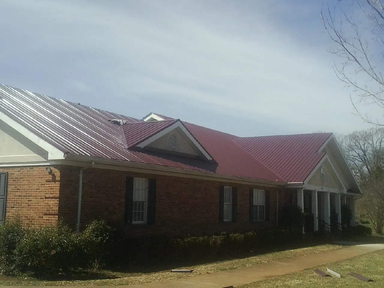 Red metal roof with gabled entries on a long brick building, from a Hail Damage Roof Repair job in Olanta