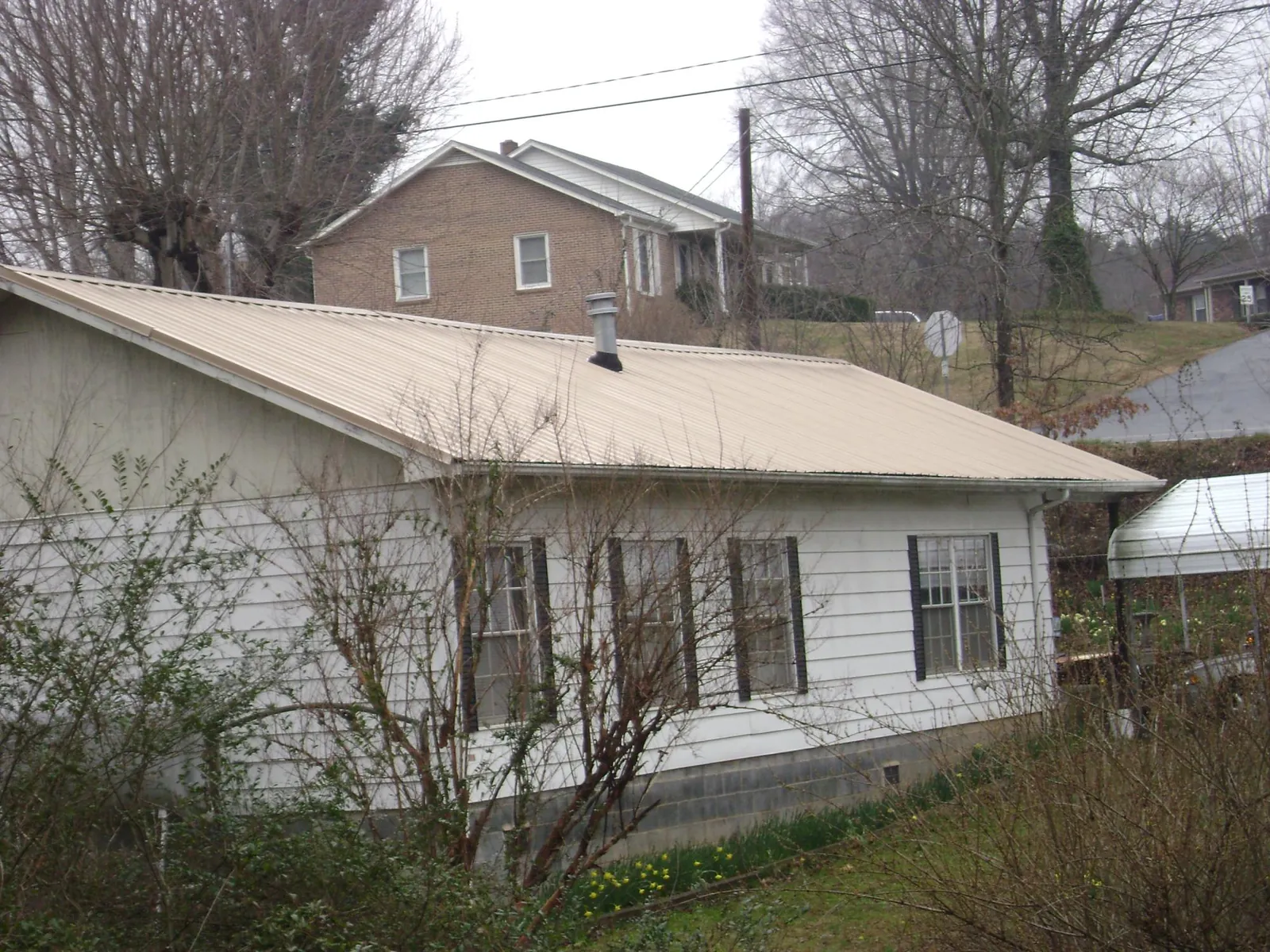 Tan metal roof on a white sided house set into a hillside — Commercial Roofing by Roofing Brothers in Olanta