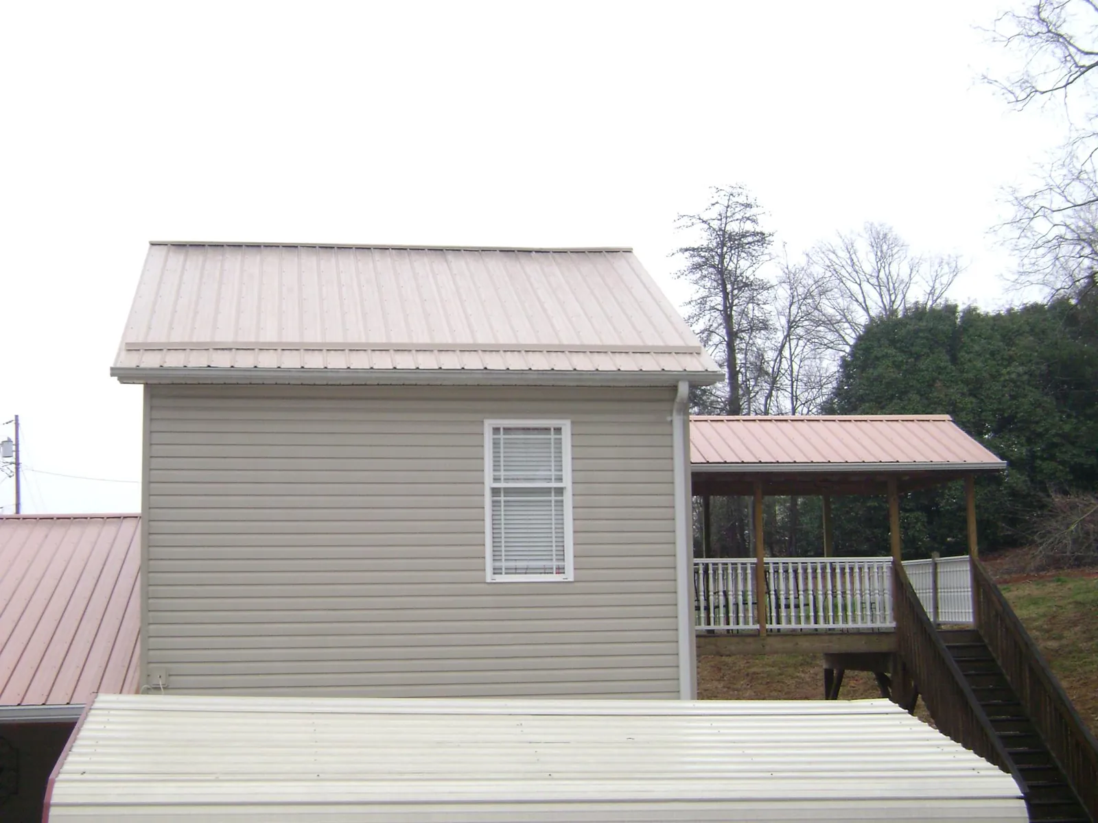 Tan metal roofs on a two story addition and attached porch, from a Roof Replacement job in Olanta